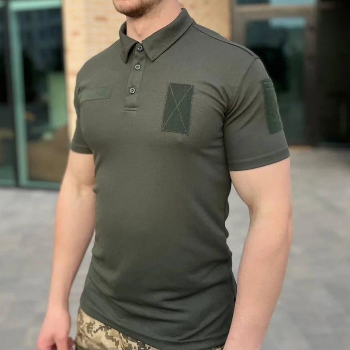 Close-up front view of a man wearing an olive tactical polo shirt with velcro patches and a chest pocket.