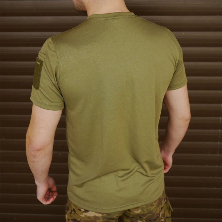 Rear view of a man wearing an olive green t-shirt with a Velcro patch on the right sleeve.