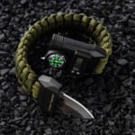 Tactical wristwatch with integrated compass and survival tools on rocky surface.