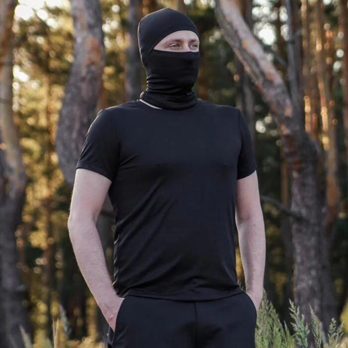 Front view of a man wearing a black t-shirt and face cover in the woods.