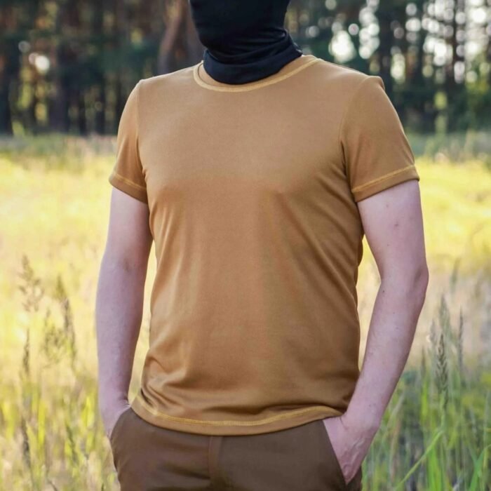 Front view of a man standing in a forest wearing a coyote brown t-shirt.