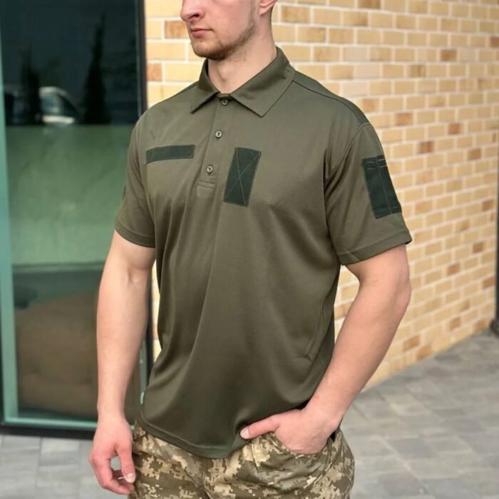 Front view of a man wearing a light olive tactical polo shirt with chest and shoulder patches.
