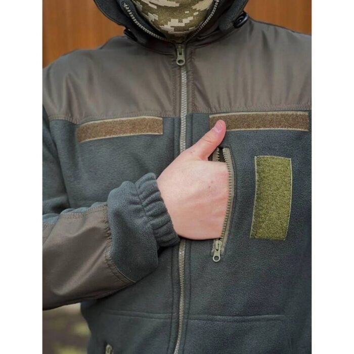 Close-up of a man's hand on the zippered pocket of a tactical fleece jacket.
