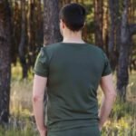Rear view of a man wearing a dark green t-shirt in a forest setting.