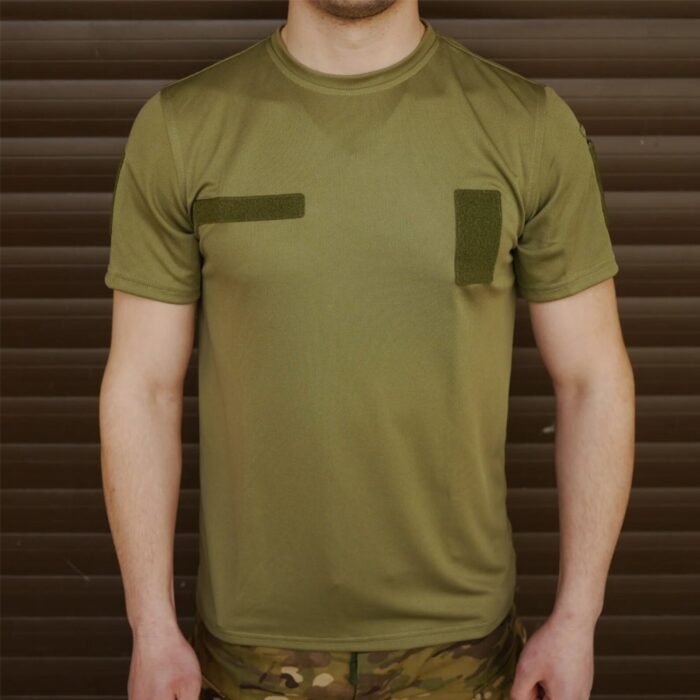 Front view of a man standing in an olive green t-shirt with Velcro patches on the sleeves.