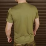 Rear view of a man wearing an olive green t-shirt with a Velcro patch on the right sleeve.