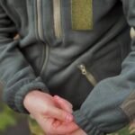 Close-up of hands with a detailed view of the zippered pocket and fabric texture on a tactical fleece jacket.