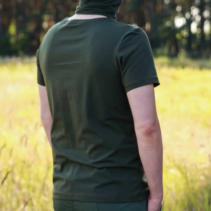 Man wearing a khaki t-shirt, viewed from behind in a sunlit meadow.