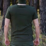 Back view of a man wearing a solid khaki t-shirt in a forest setting.