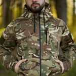 Front view of a man in Ukrainian multicam uniform with jacket fully zipped and hood up in a forest.