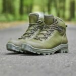 A pair of olive tactical shoes placed on a road in a forest setting, showcasing their rugged design and high-quality leather construction.